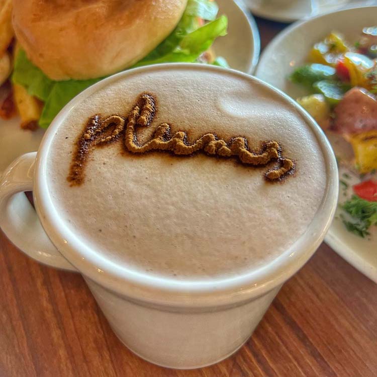 A dusting of spices atop a latte brimming with foam spells the word "plums" in cursive lettering. 