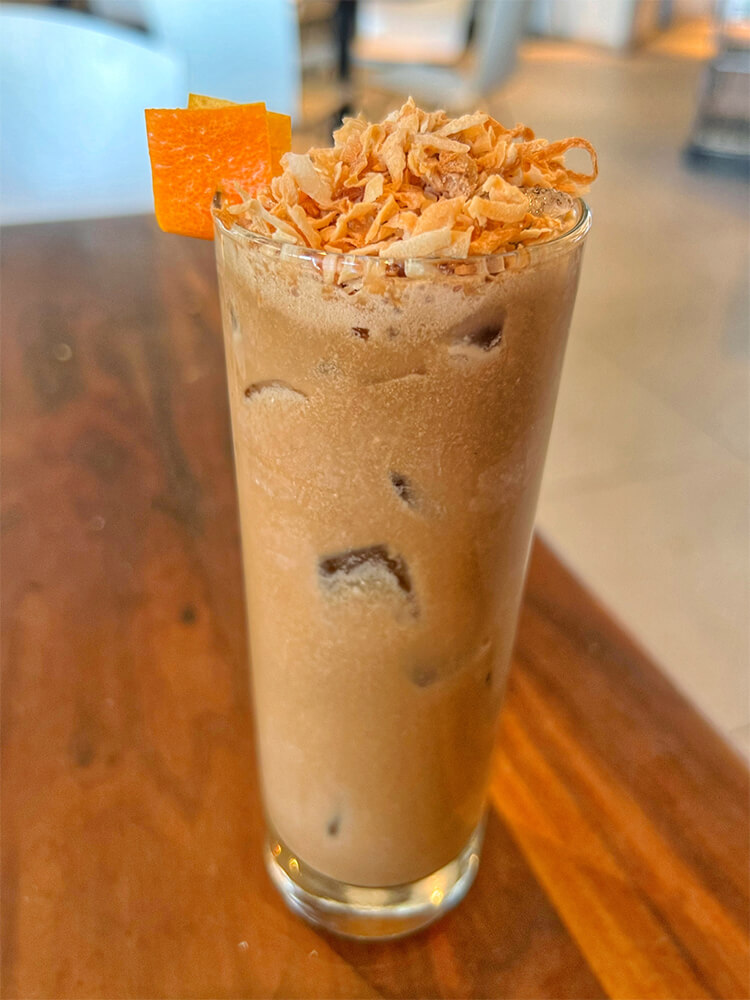A Hazelnut espresso cocktail topped with toasted coconut shavings and garnished with orange zest.