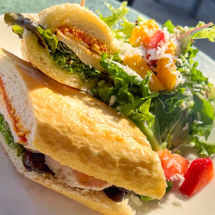 Tuscan chicken, sun dried tomatoes, basil pesto, mozzarella tucked into a fresh baguette next to a side salad of mixed greens and fresh fruit. 