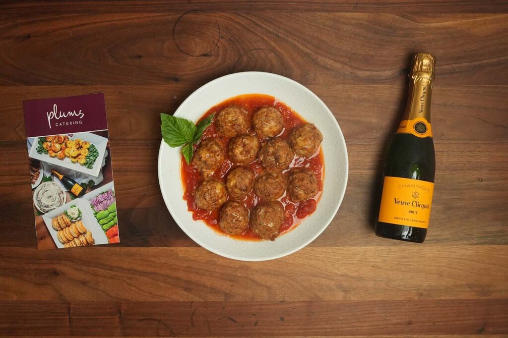 Meatballs in tomato sauce beside champagne and catering brochure