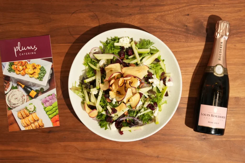 Apple cranberry salad beside rosé bottle and catering brochure
