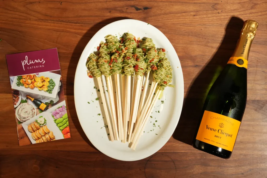 Pesto pasta skewers beside champagne bottle and catering brochure